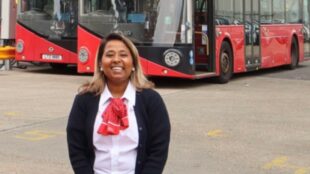 Koli Begum smiling in front of a row of famous red London buses.