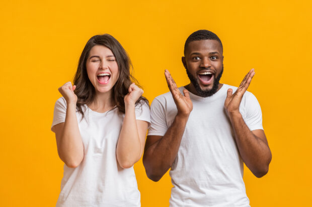 Overjoyed girl emotionally clenching fists with closed eyes while her boyfriend is raising his hands